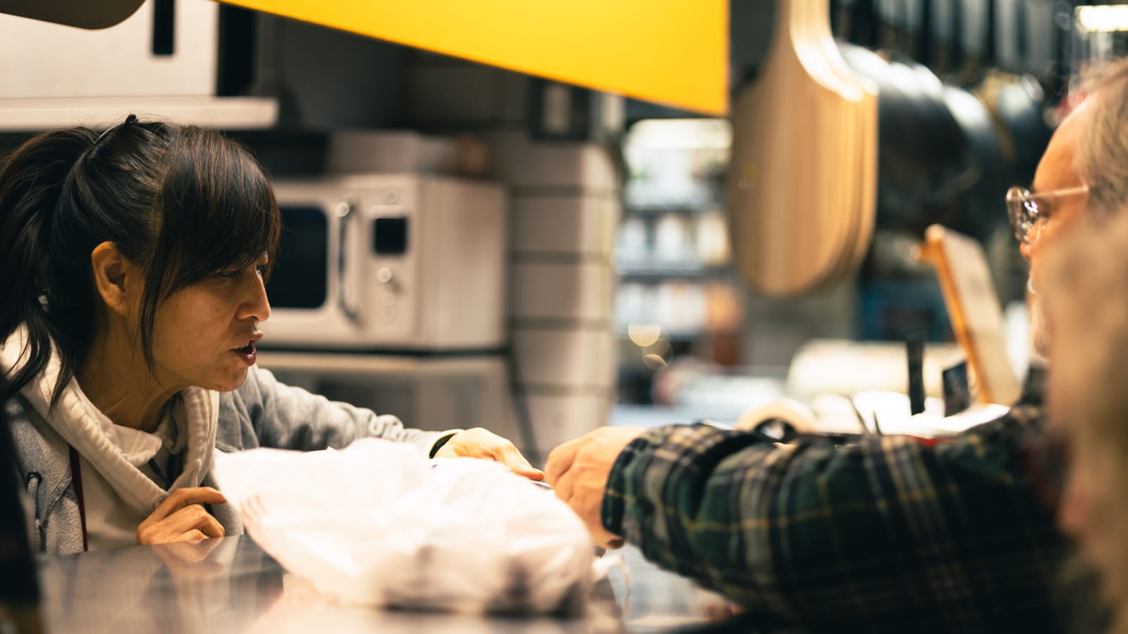 A seller handing a wrapped order to a customer across a market counter.